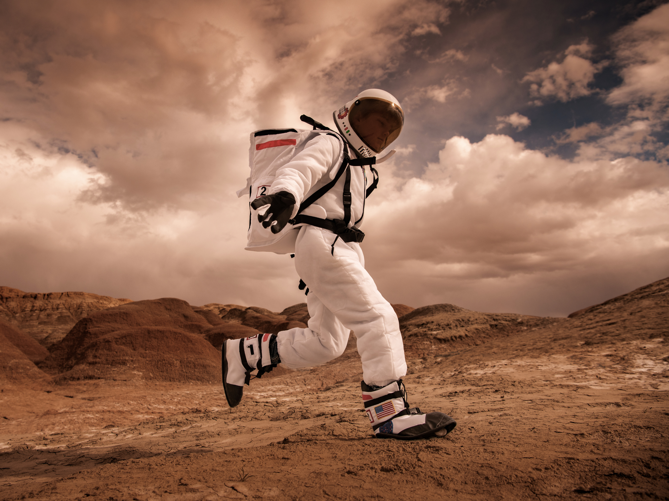 Close-up portrait of an astronaut with a reflective visor, dominated by warm orange and amber tones.